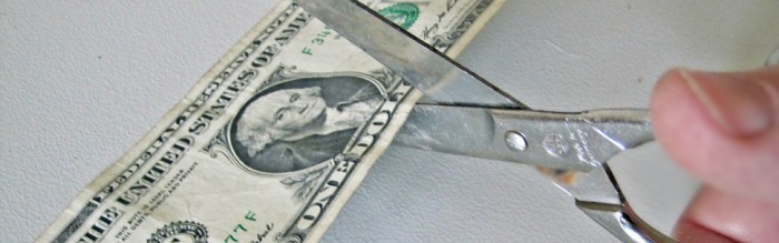 scissors cutting through a dollar bill